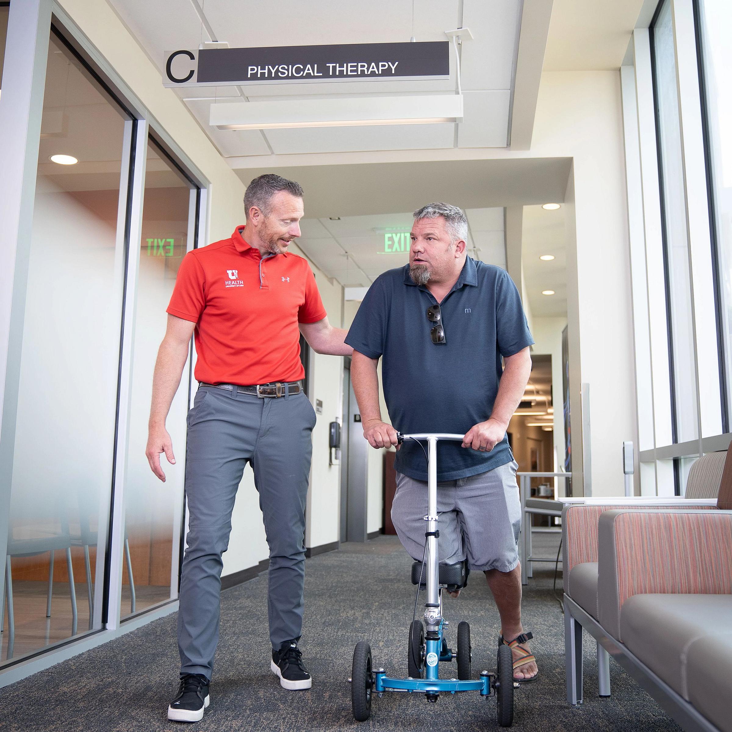 Jason Miller, physical therapist, helps a male patient down the hallway