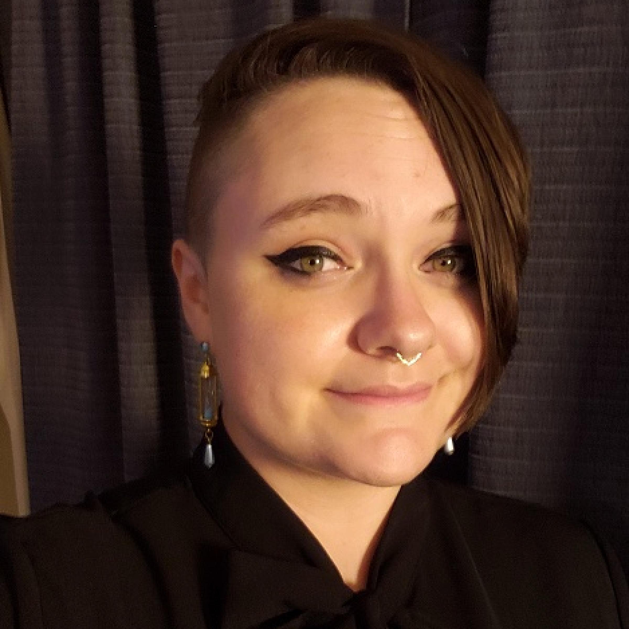 Hannah Hinchman has short brown hair with one side shaved and wears a black blouse.