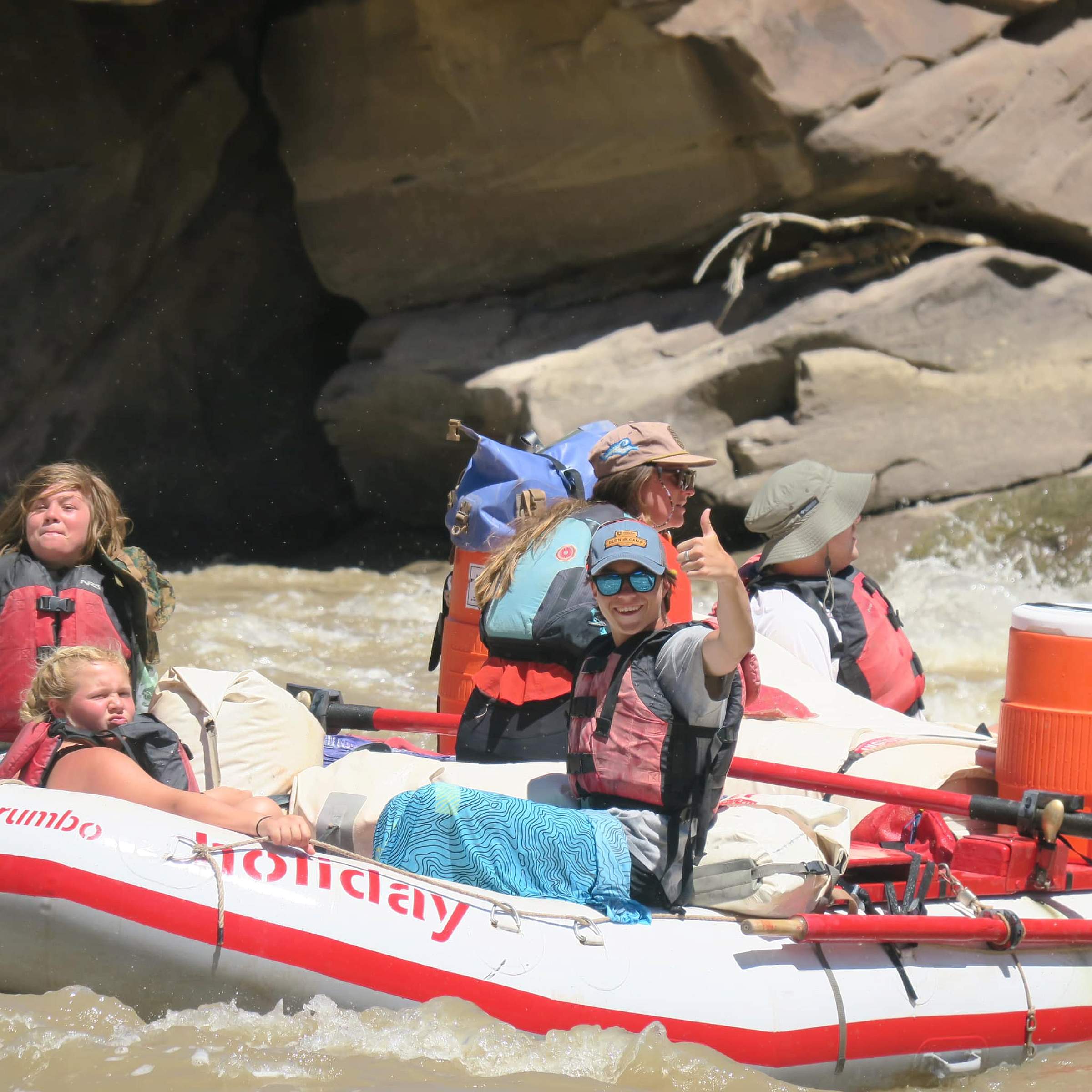 Person wearing sunglasses and rafting gives thumbs up to the camera