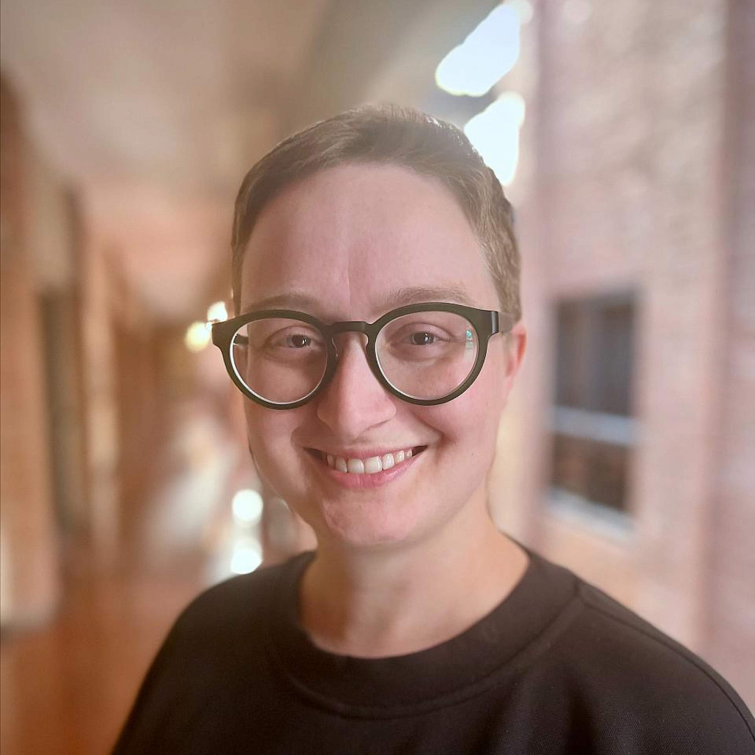 Person with short medium brown hair and glasses smiles at the camera