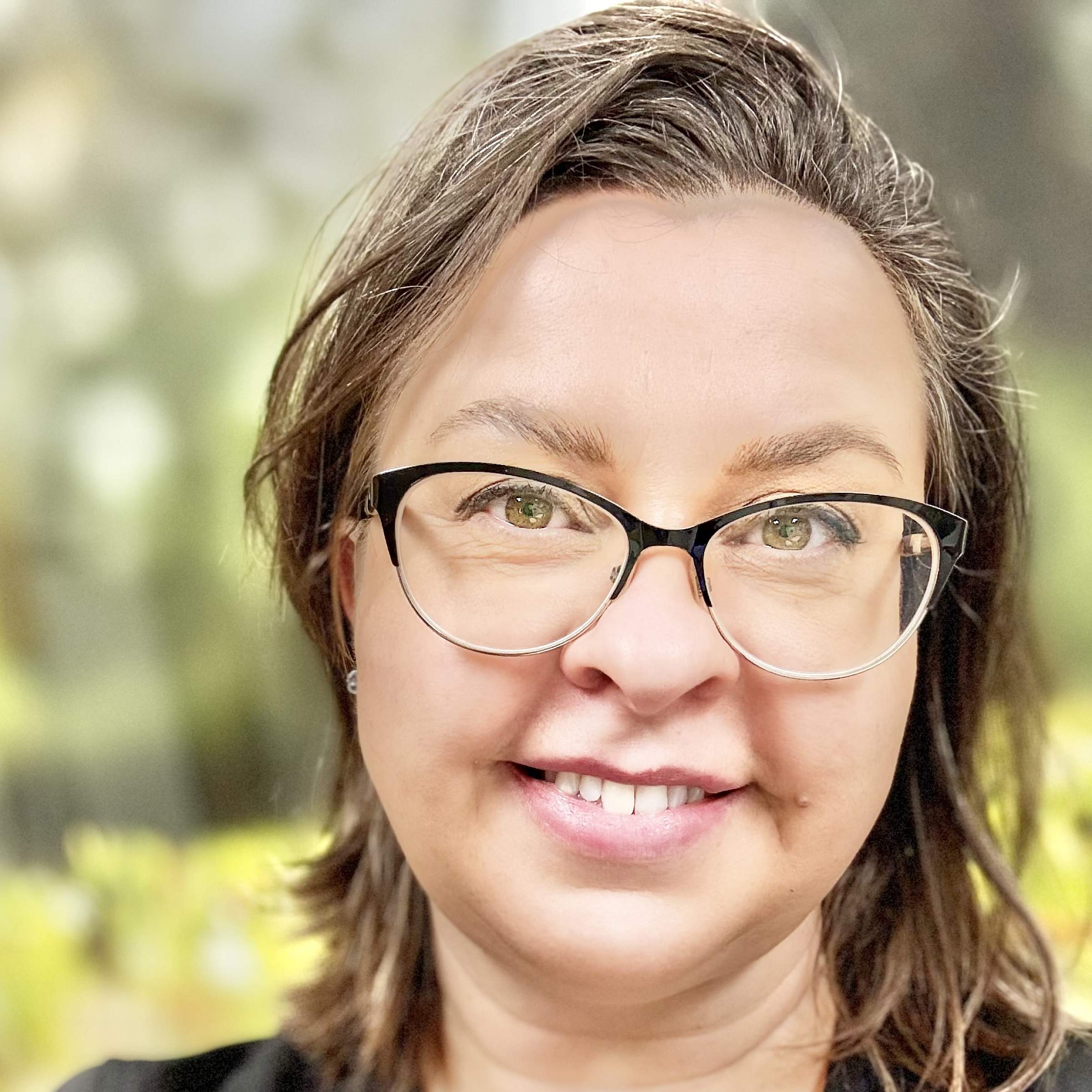 A woman with glasses and shoulder length brown hair smiles for a profile picture