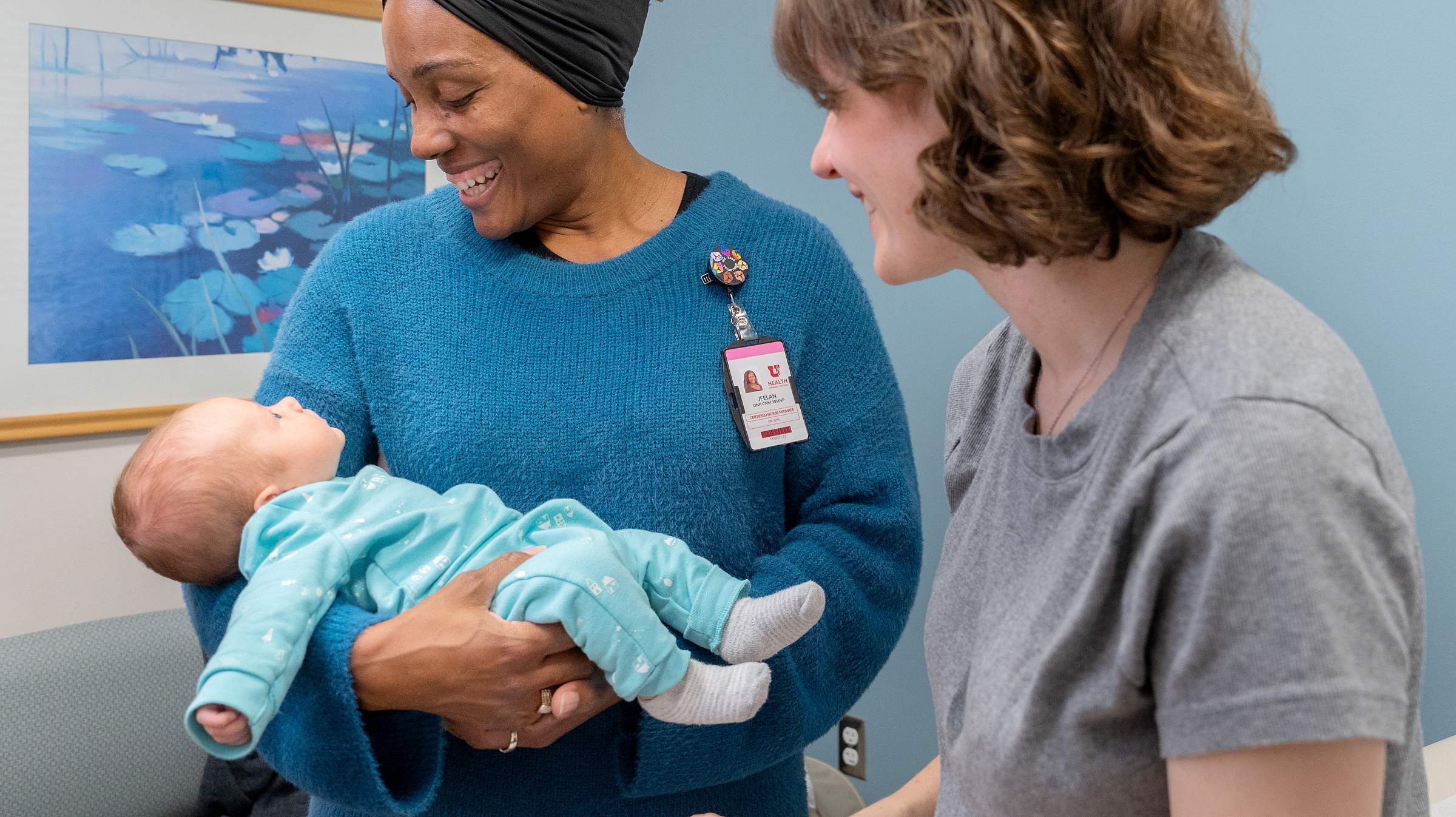 Nurse midwife female with dark skin tone looks down at baby and smiles. 