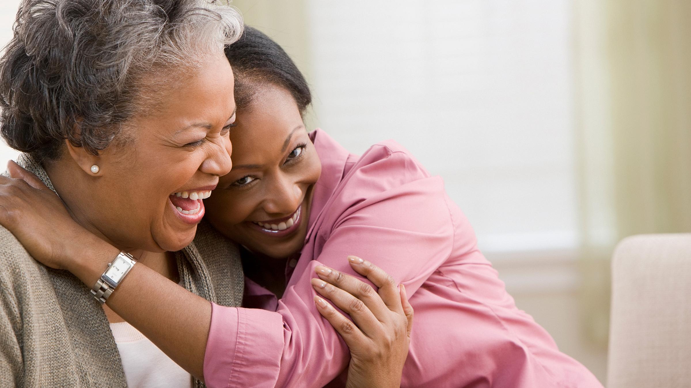 Middle aged woman with dark skin hugging an older woman who is laughing