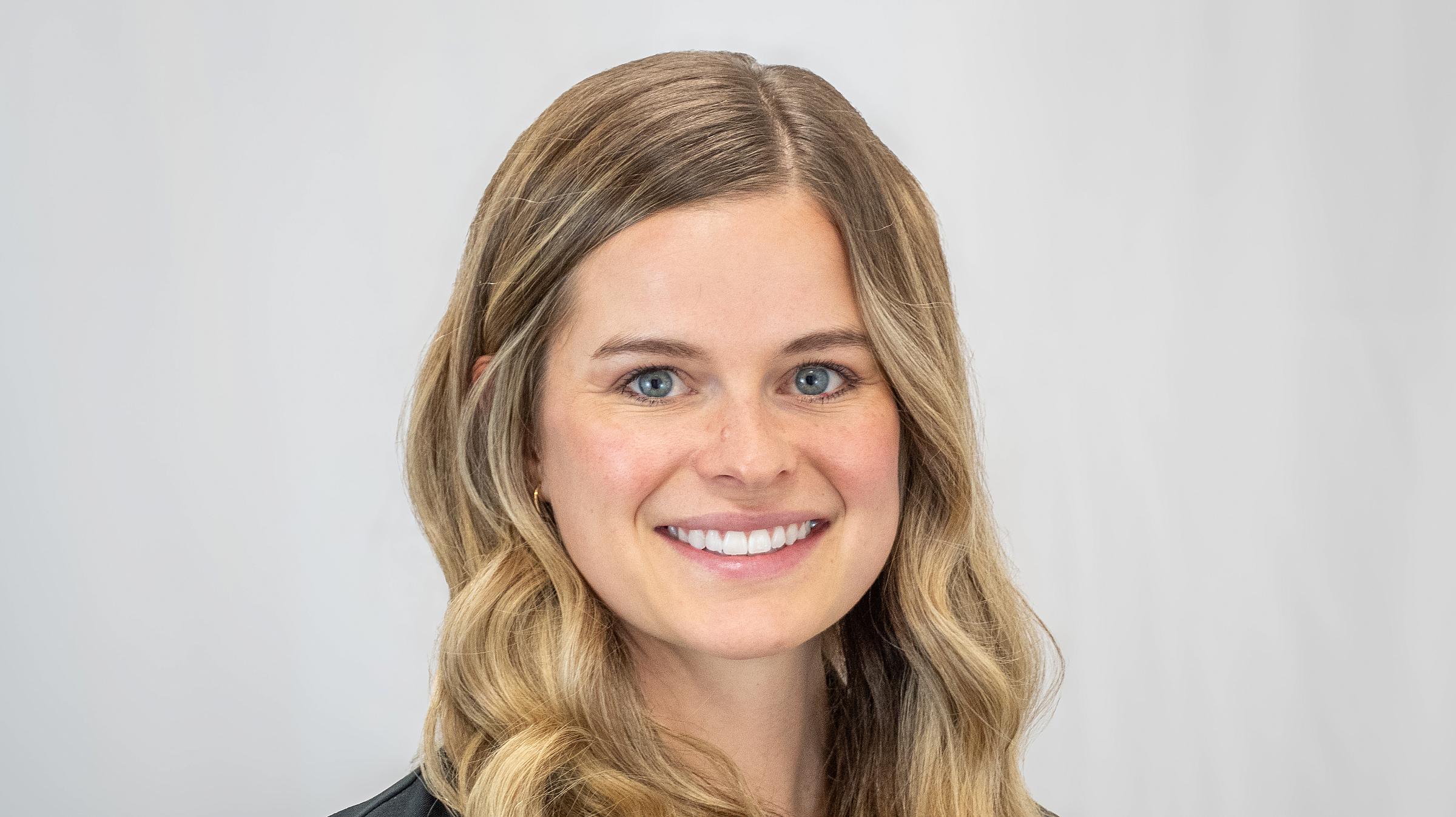 Alicia May has long, wavy blonde hair and wears a black blazer.
