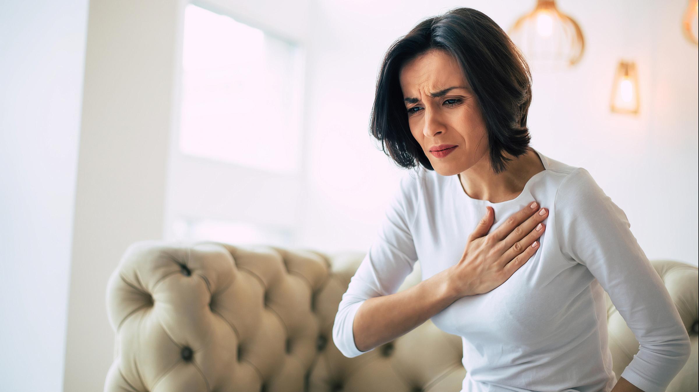 Woman sitting on couch with a hand on her heart